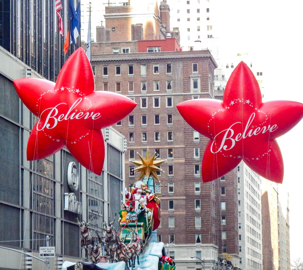 two red star-shaped parade balloons that say "believe" on them at the macys thanksgiving day parade