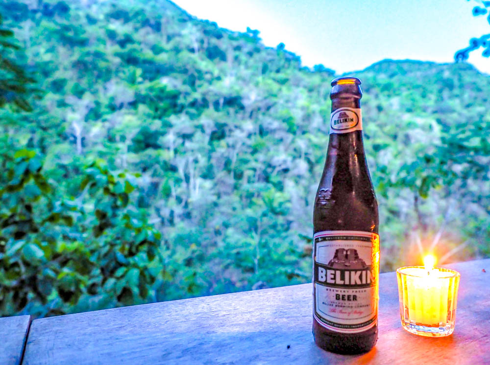 bottle of belikin beer next to a candle on a ledge overlooking the jungle at dusk