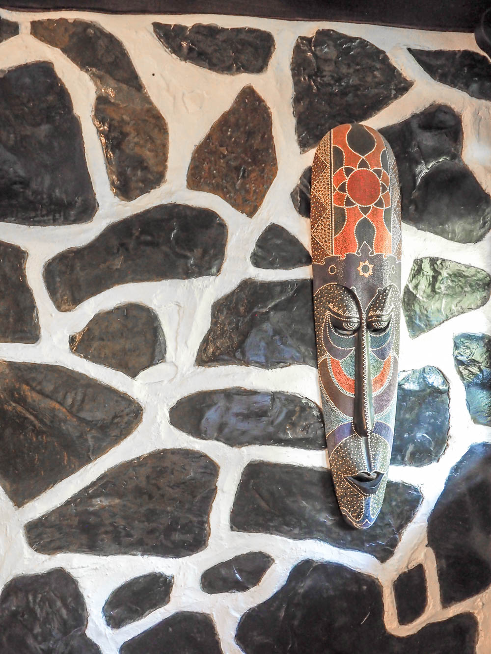 artistic mask hanging on a black and white stone wall