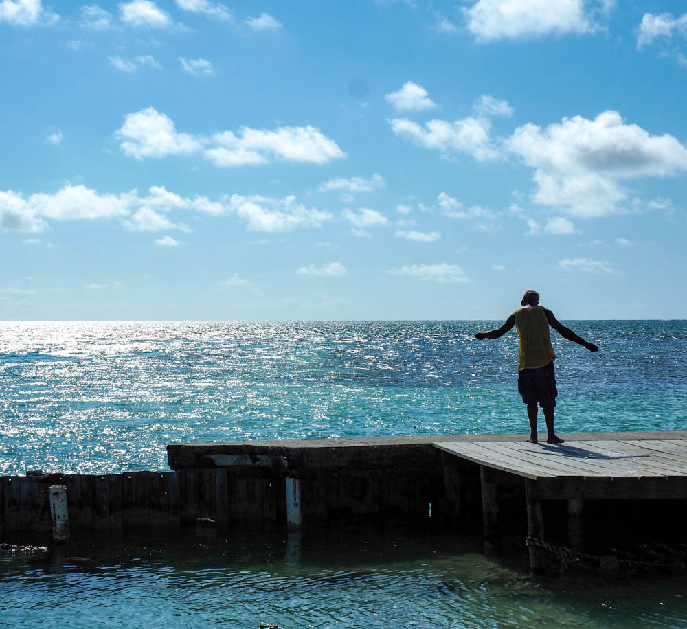 man fishing on a dock over a turquoise ocean