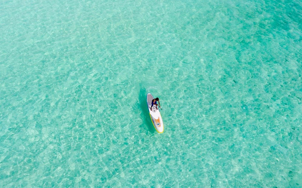 man stand-up paddle boarding in turquoise water seen from above