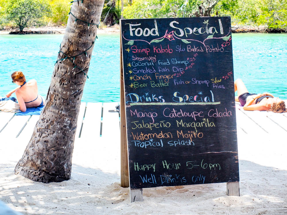 food menu under a palm tree next to a turquoise ocean in belize