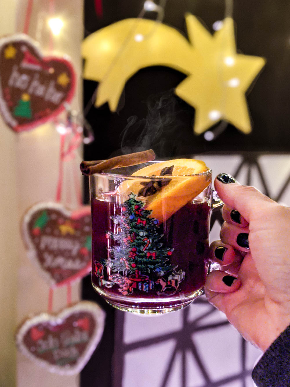 glass of gluhwein in a cute christmas mug in front of lebkuchenherzen and christmas star