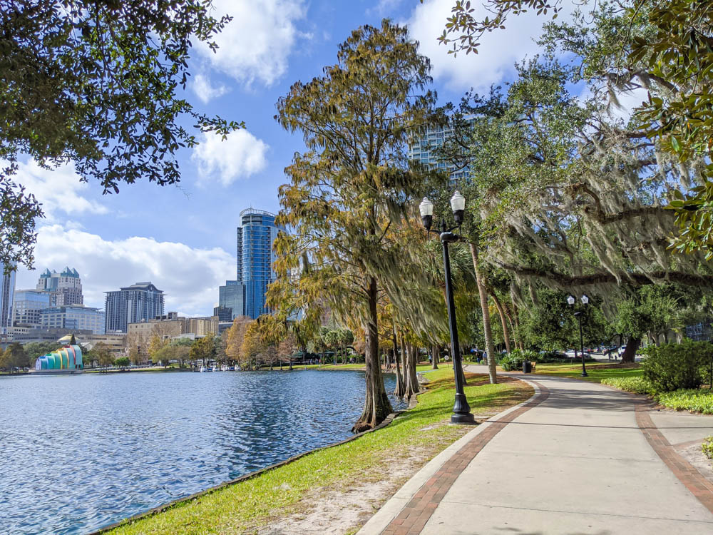 lake in front of urban skyline with walking path covered in spanish moss