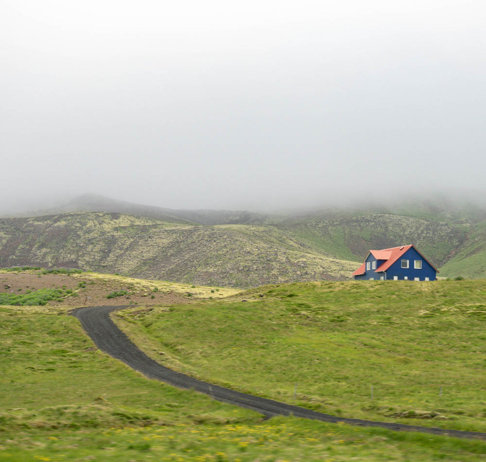 small blue house with orange roof in a grassy field with fog