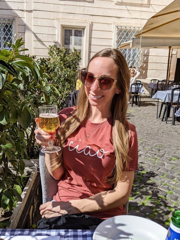 girl in Italian cafe holding a beer and wearing a shirt that says Ciao on the front