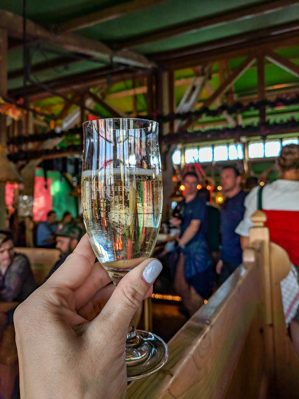hand holding up glass of champagne inside oktoberfest beer tent
