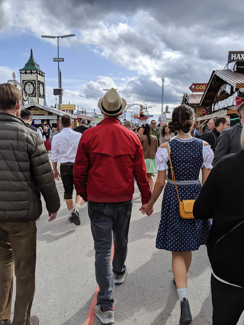 a girl in a blue dirndl and a man in a red jacket walking through oktoberfest in munich