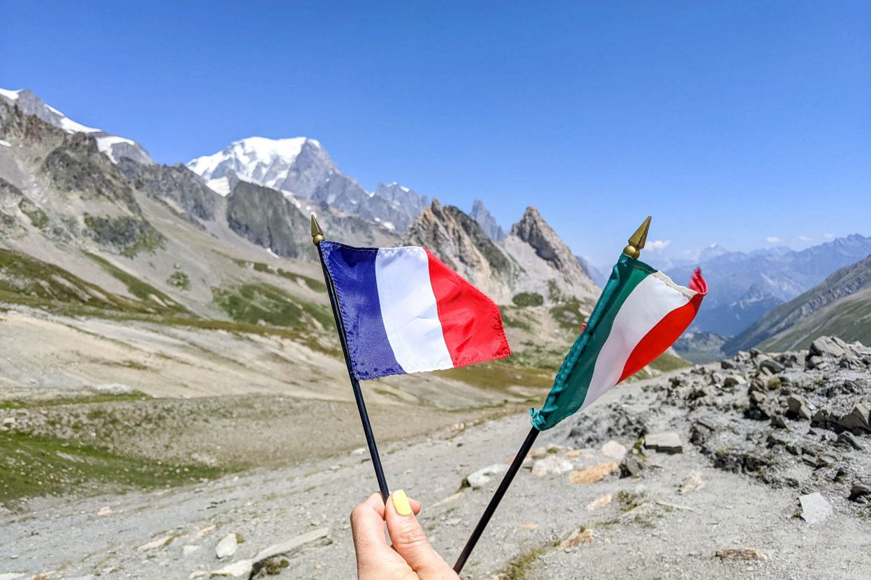 hand hold and a france and italy flag in front of some mountains
