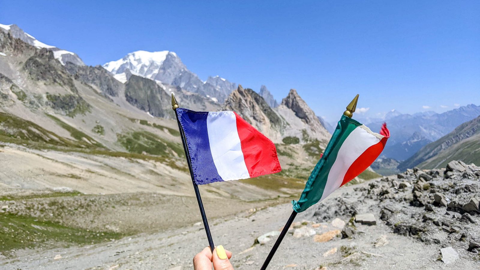 hand hold and a france and italy flag in front of some mountains