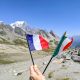 hand hold and a france and italy flag in front of some mountains