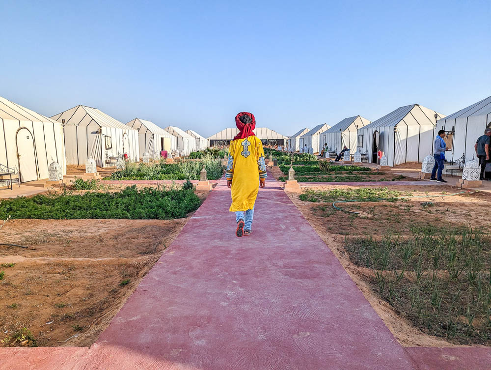 a man in a yellow shirt with red headscarf walking between a long lines of white tents