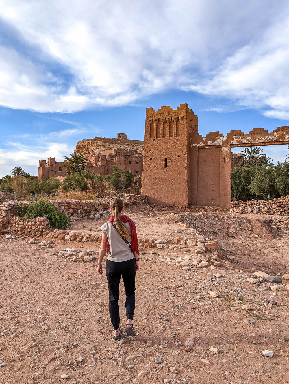 woman in black pants and tan shirt standing in front of a desert building