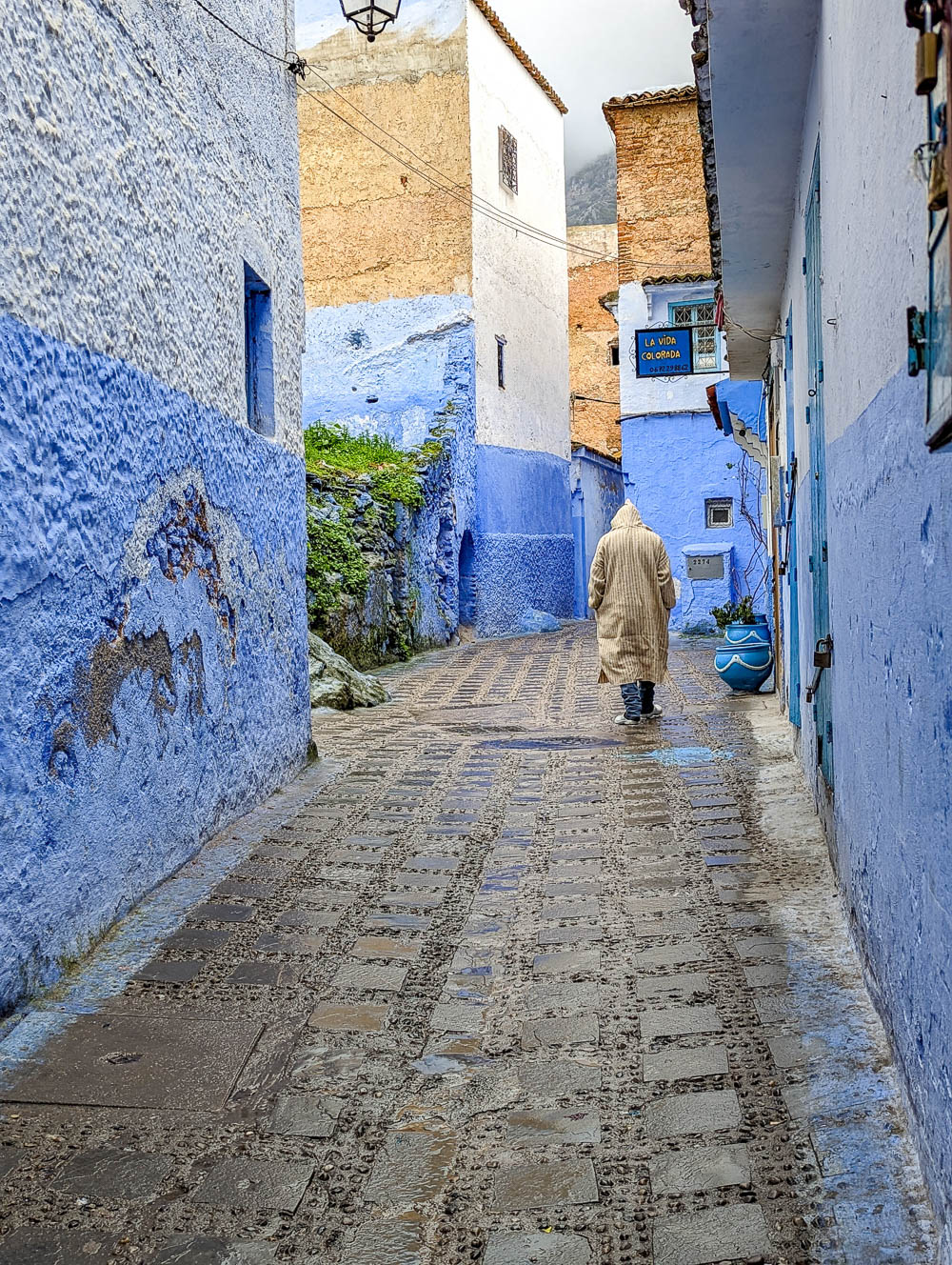 man in a long beige robe walking down a blue alleyway