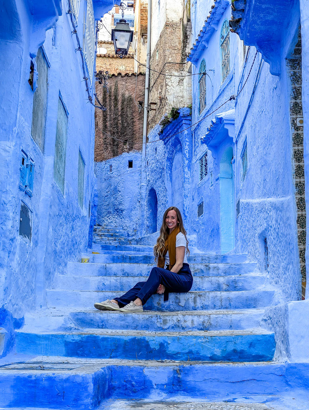 woman in blue pants sitting in an entirely blue alleyway and staircase