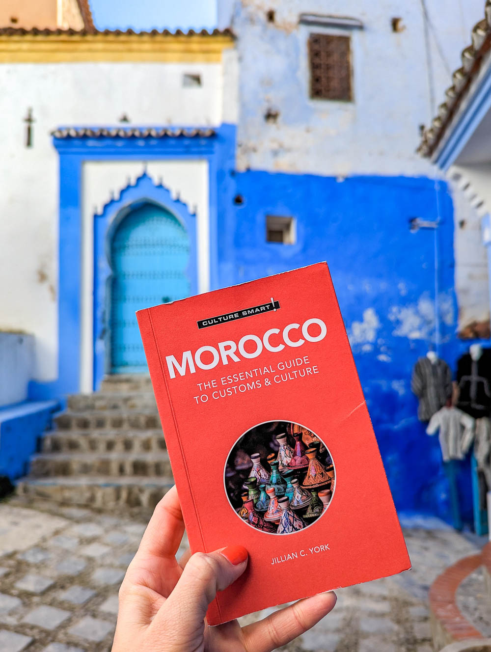 hand holding up a red morocco guide book in front of a blue door