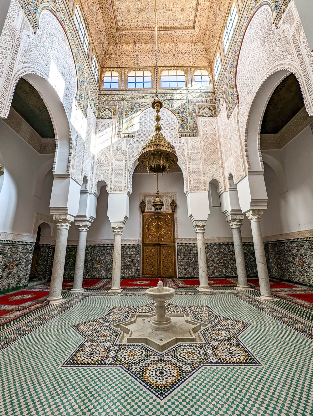 intricately decorated room of mosaics, wood carvings, windows, and a fountain in the middle