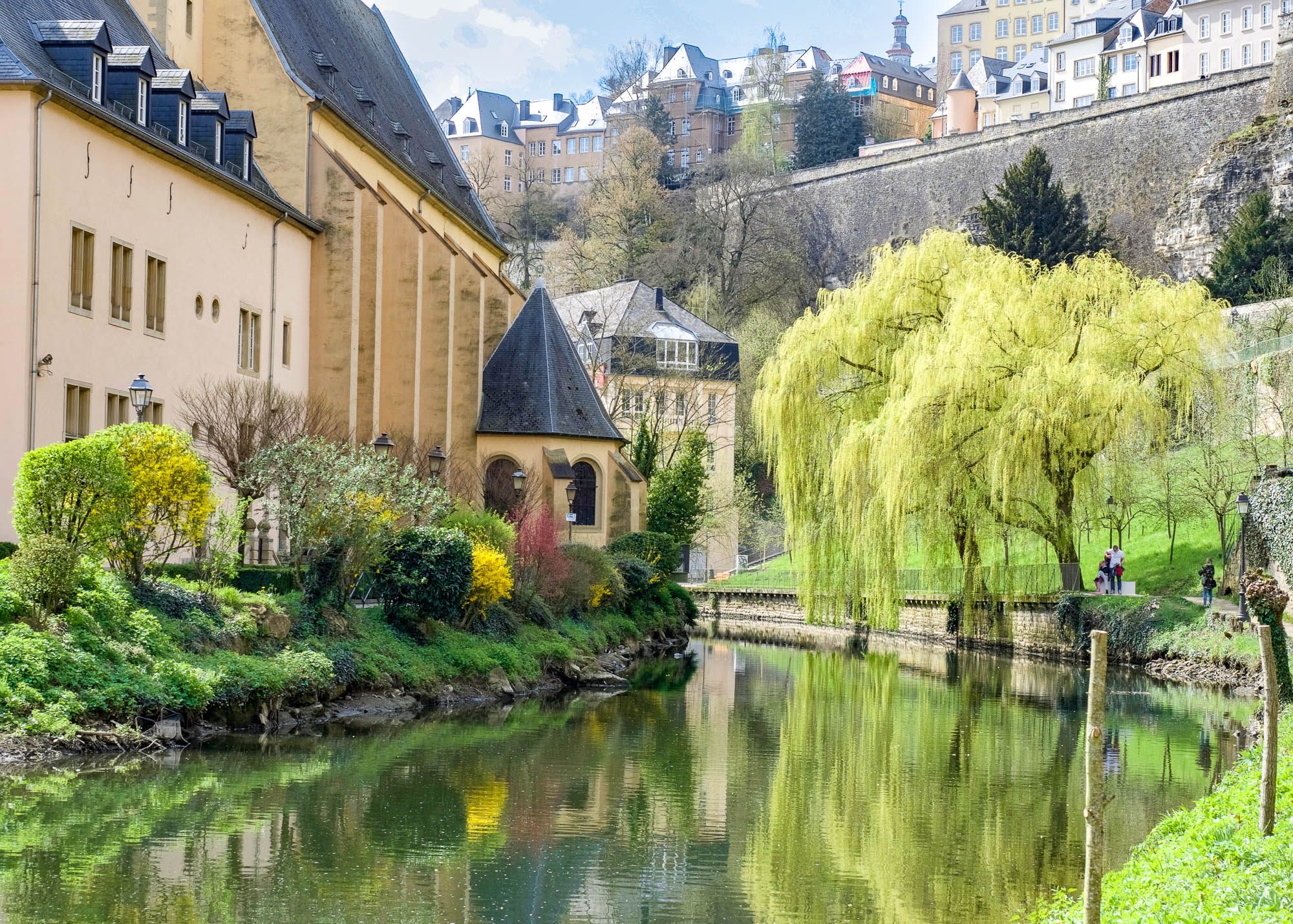 a small river with a yellow building on one side and big willow tree on the other