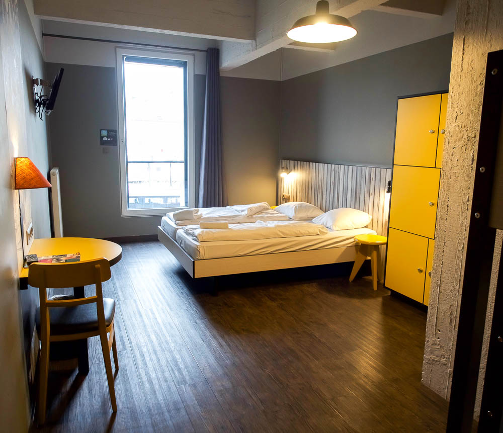 large hotel room with plain white beds and yellow cabinets