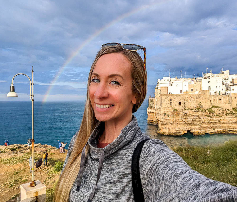 woman in front of a blue ocean with a rainbow going over her head