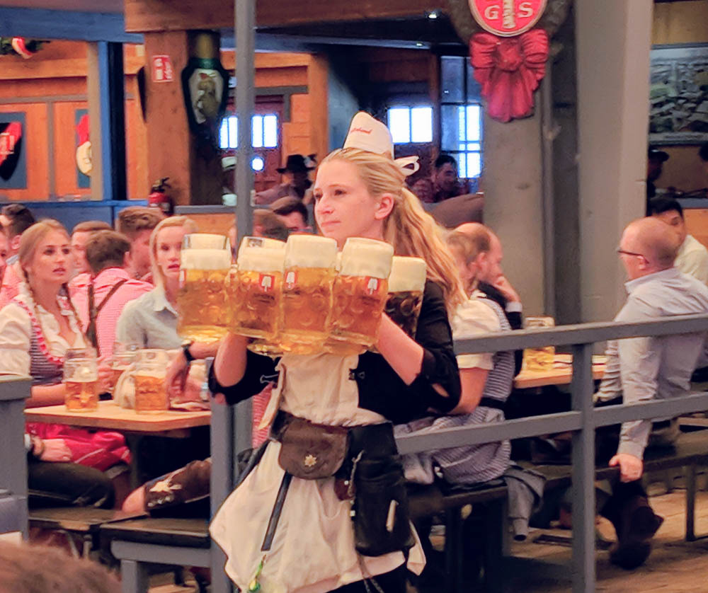 woman carrying 10 large beers at once inside a beer tent