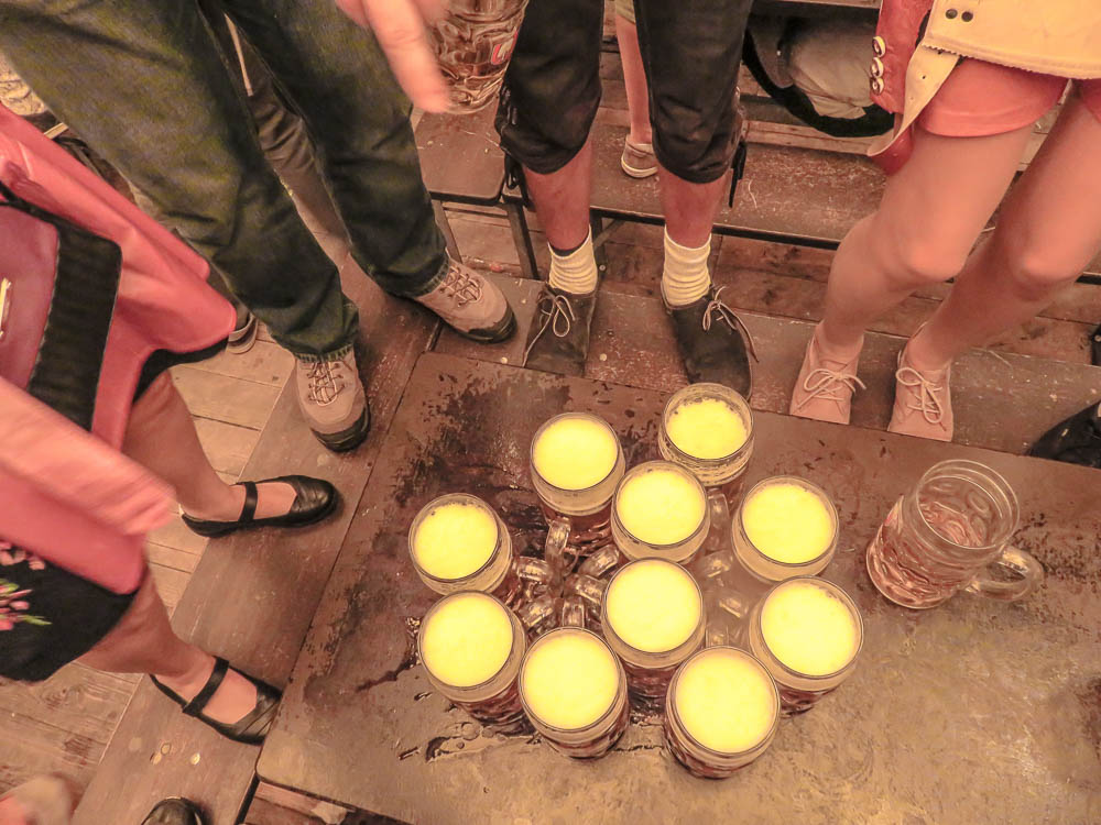 looking down at a table full of beer mugs while people stand on the bench around them