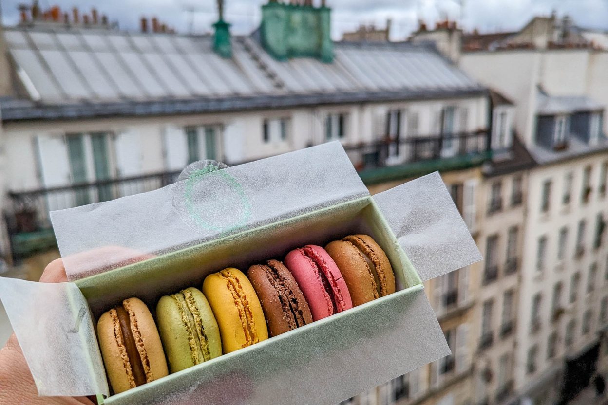 hand holding box of colorful macarons in front of a Paris skyline