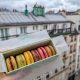 hand holding box of colorful macarons in front of a Paris skyline