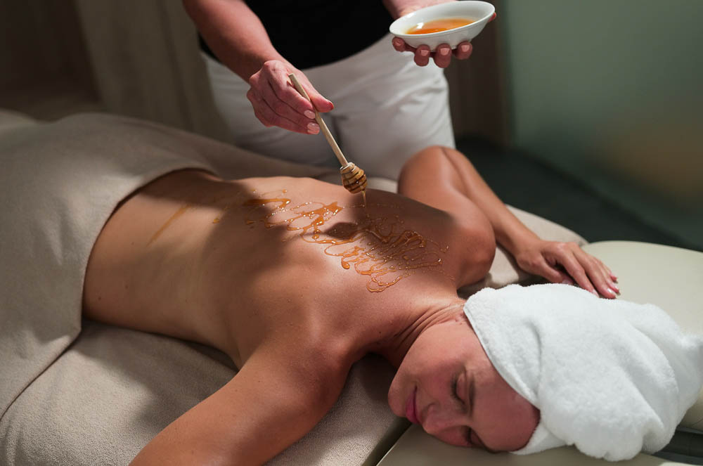 woman on a massage table getting honey drizzled on her back