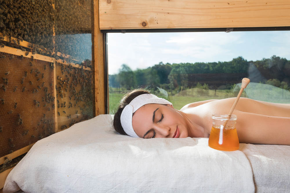 woman laying on a bed next to some beehives and a jar of honey