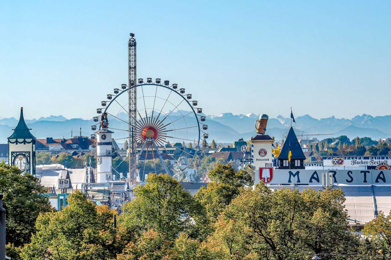 view of oktoberfest beer tents and ferris wheel with alps in the background