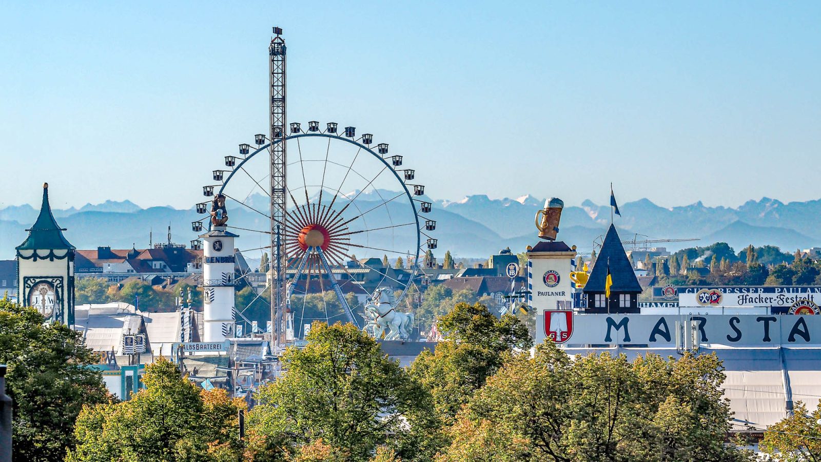 view of oktoberfest beer tents and ferris wheel with alps in the background