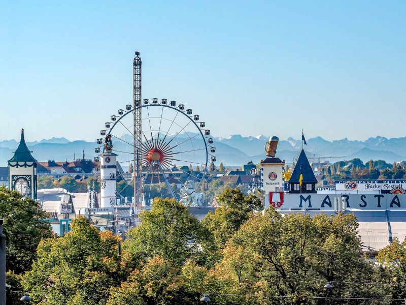 view of oktoberfest beer tents and ferris wheel with alps in the background