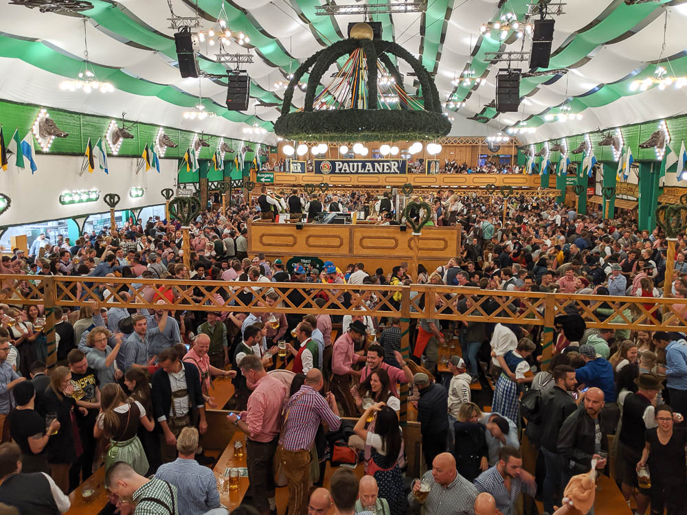 inside a large crowded oktoberfest beer tent under green and white streamers