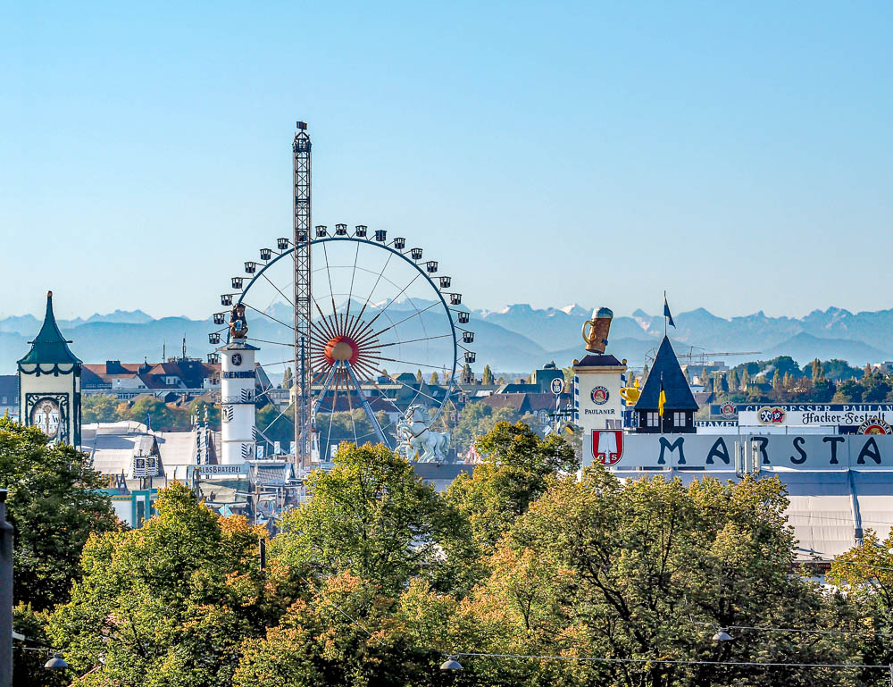 view of oktoberfest beer tents and ferris wheel with alps in the background