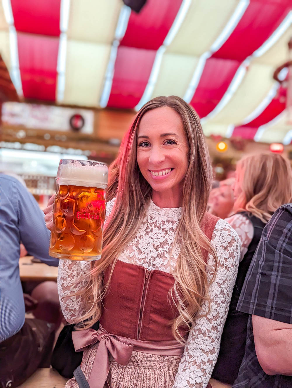 woman in lace shirt holding a large beer under a red and white striped tent