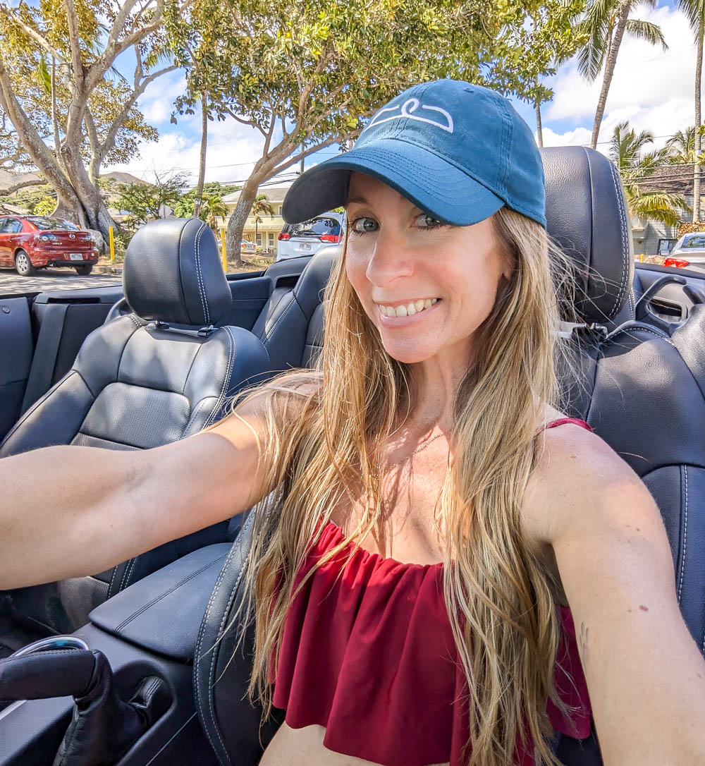 woman in red bathing suit and blue hat driving in a convertible