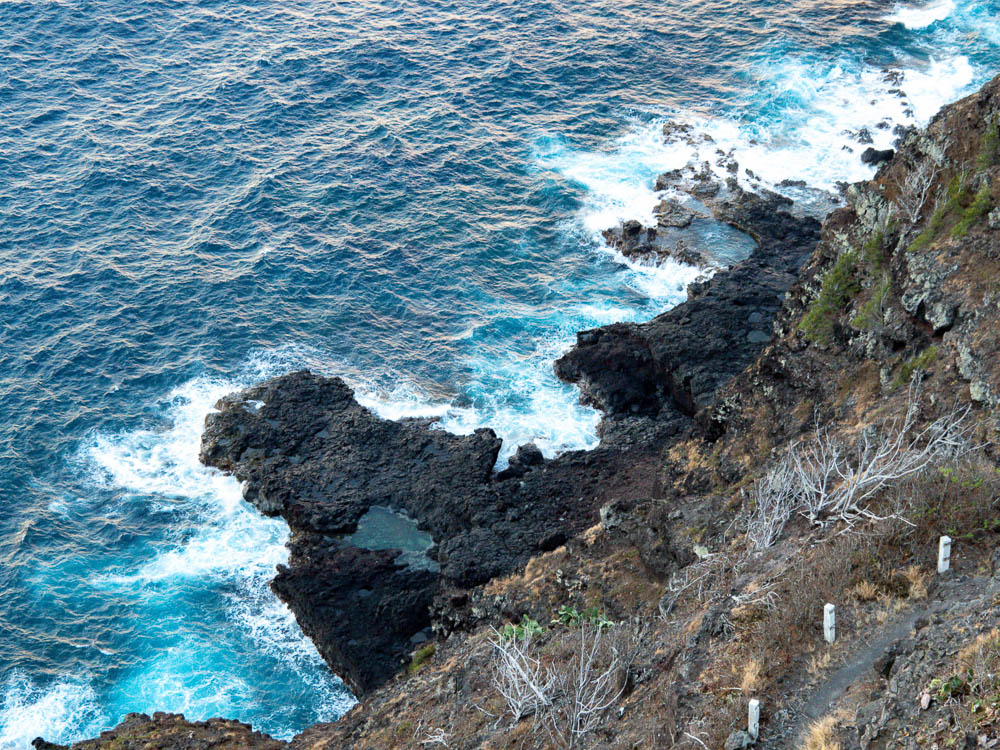 looking down on blue water hitting against black lava rocks