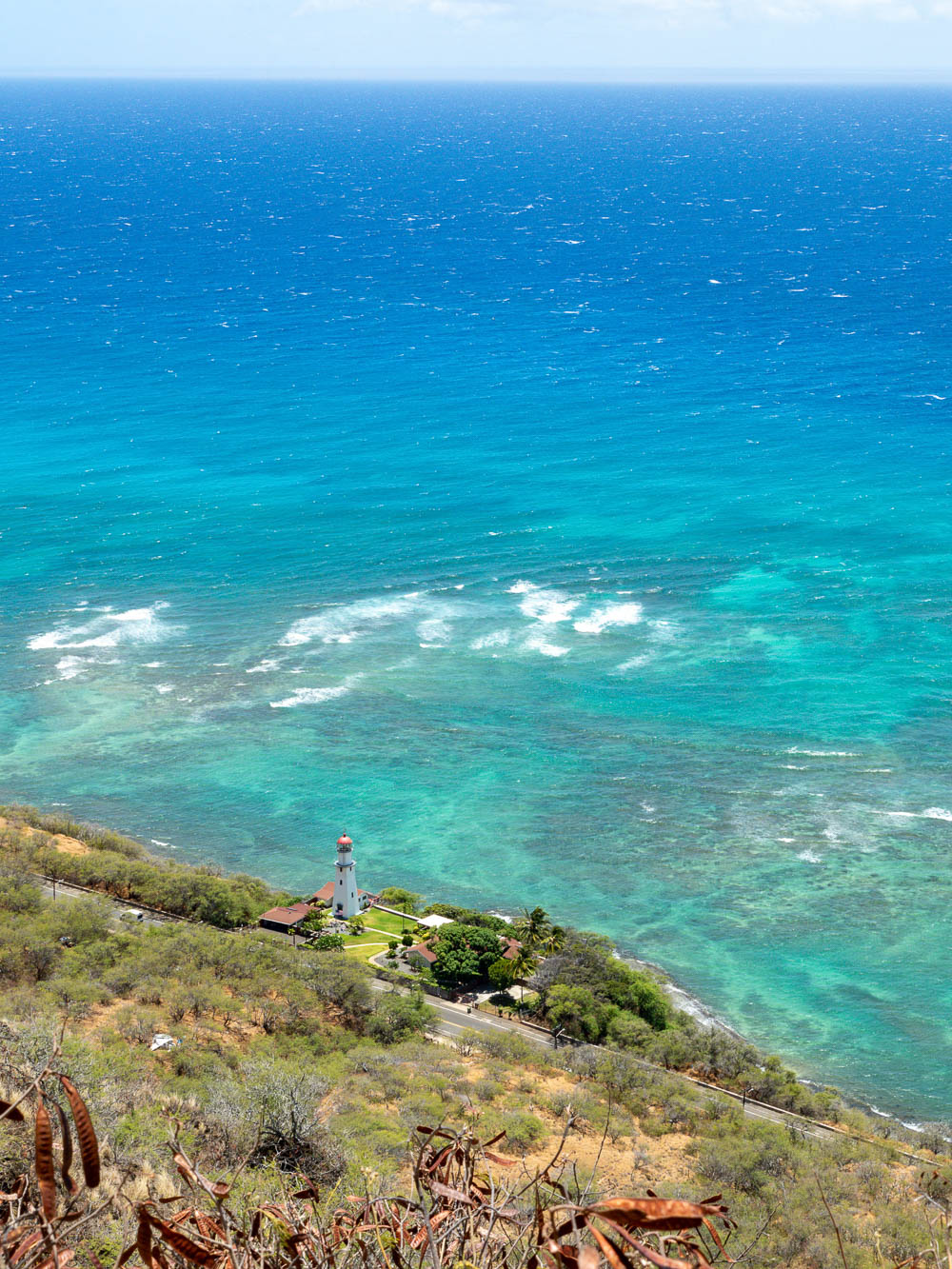 looking down on a white lighthouse next to a turquoise ocean