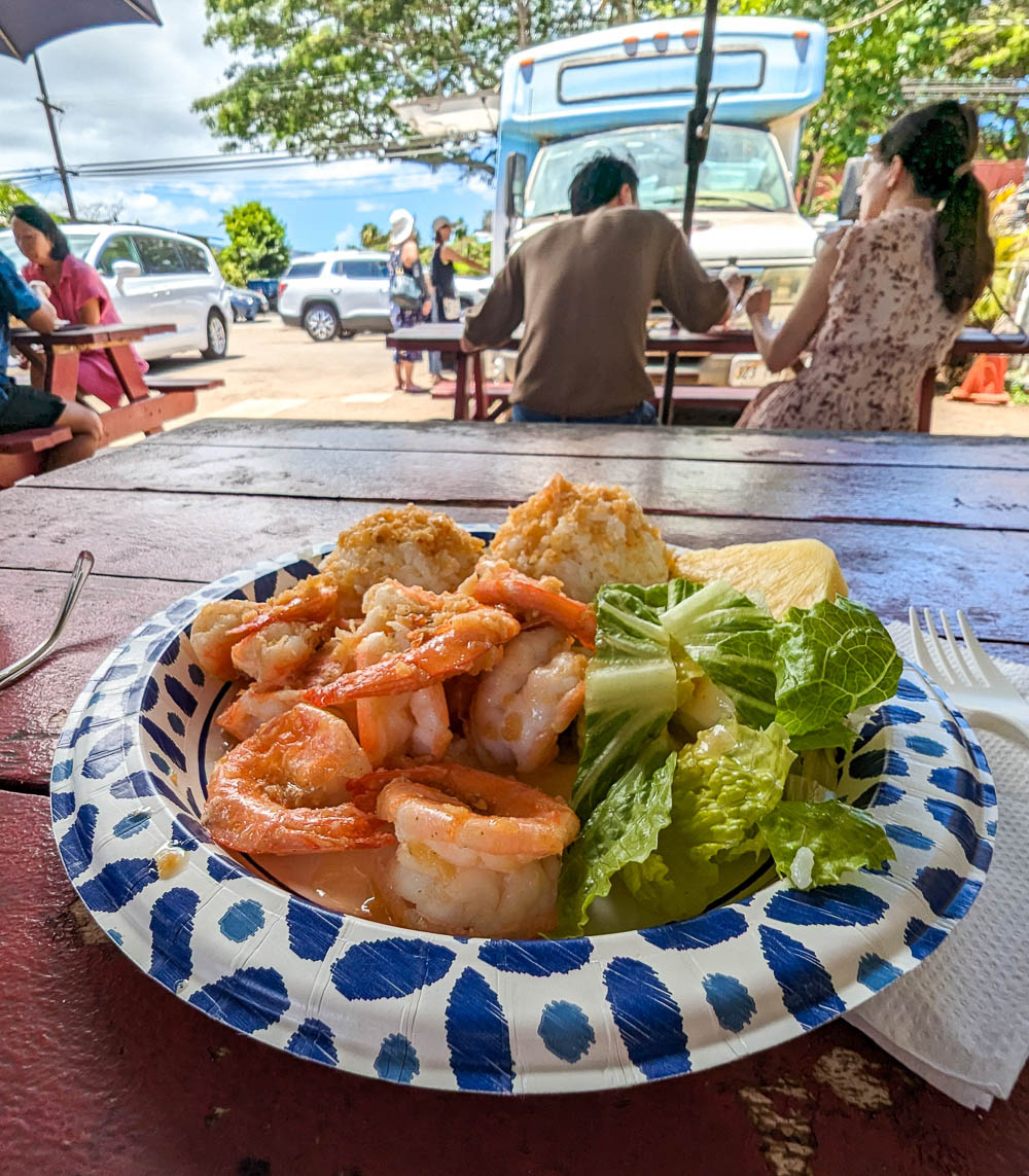 plate of shrimp with lettuce and pineapple on a picnic table next to a truck