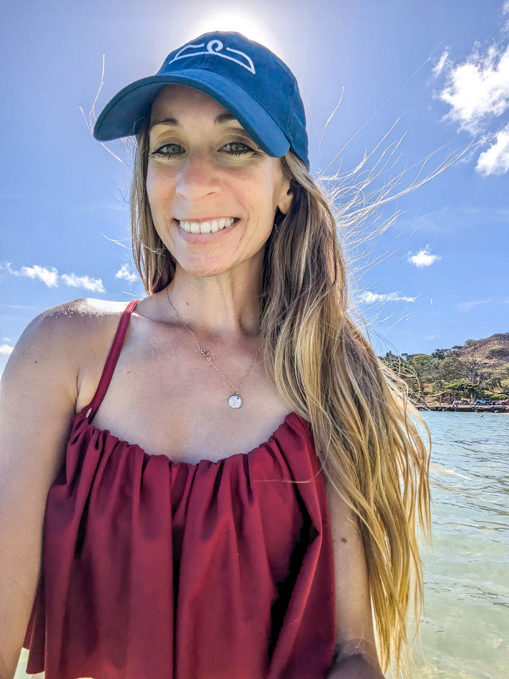 selfie of a woman in the sun wearing a red bathing suit and blue hat