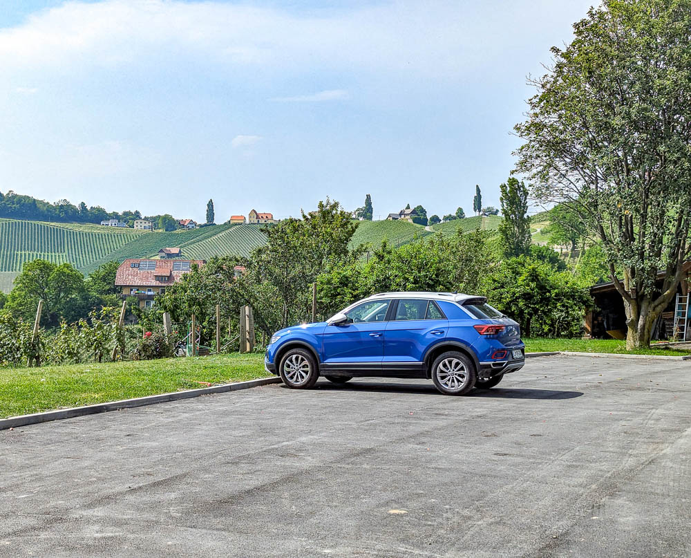 blue car in an empty parking lot next to some vineyards