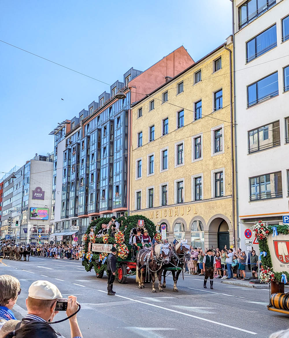 horse-drawn carriage going down a city street lined with people and colorful buildings