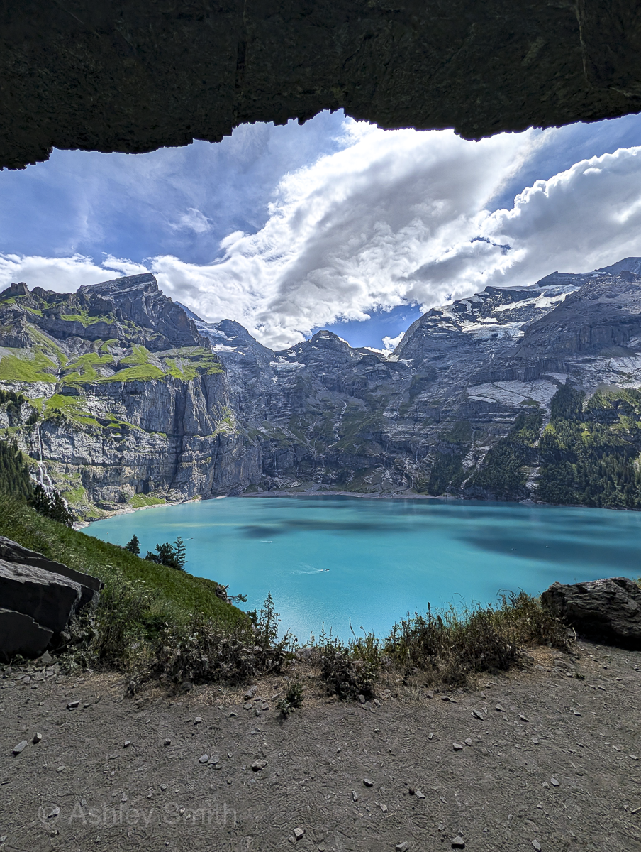 turquoise lake surrounded by green meadows and snowy mountains