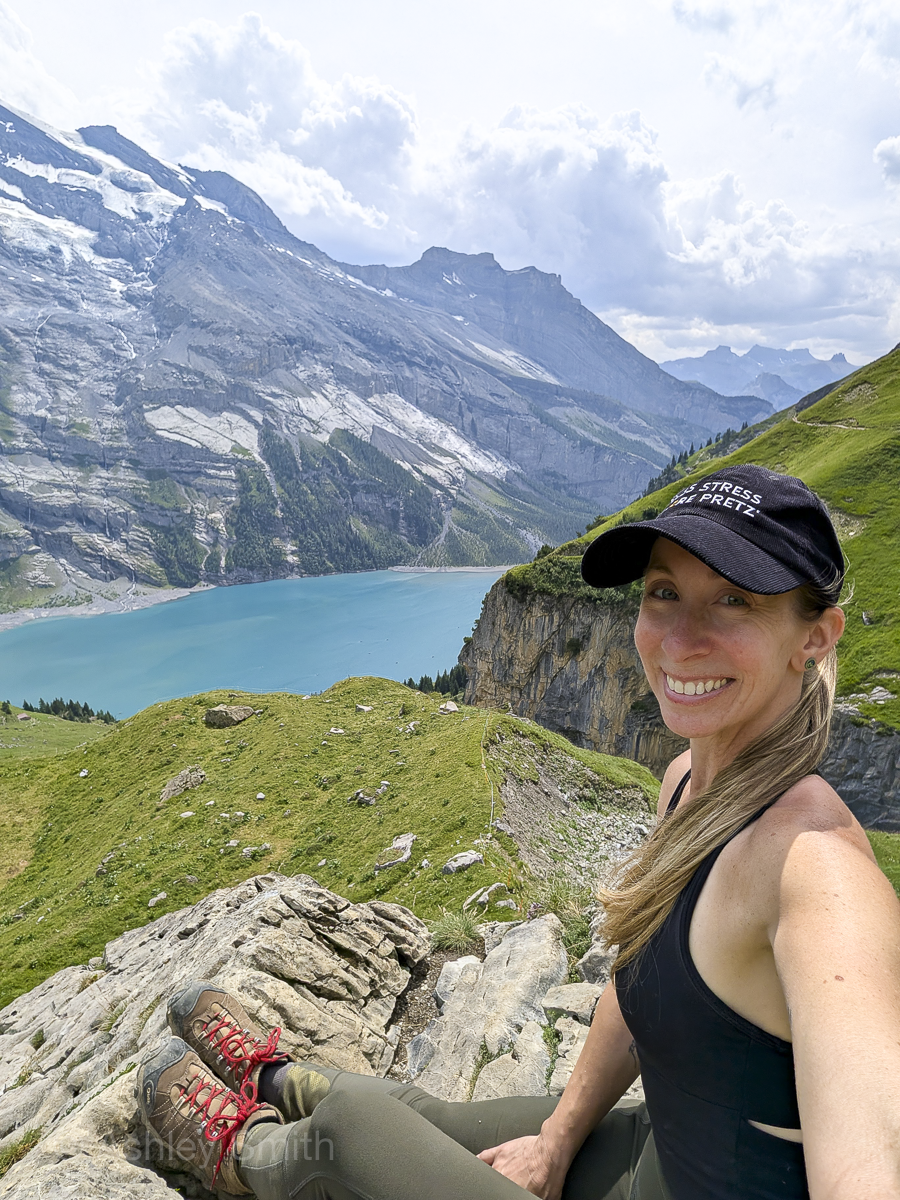 woman taking a selfie in front of a lake surrounded by mountains