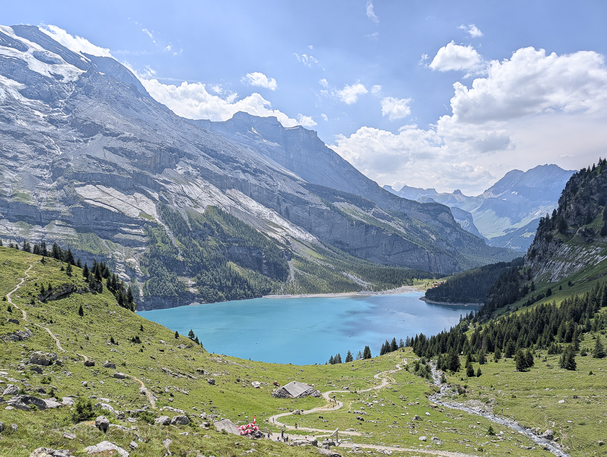 turquoise lake surrounded by green meadows and snowy mountains