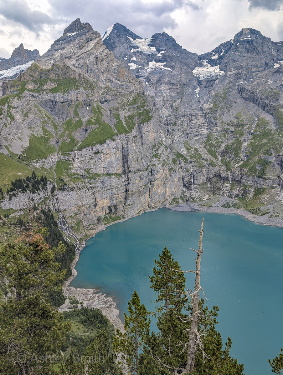 turquoise lake surrounded by green meadows and snowy mountains