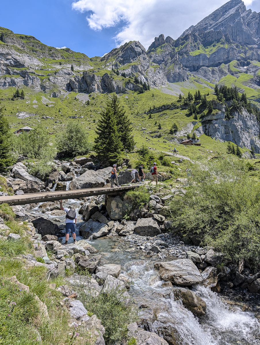people walking on a bridge over a stream in the mountains
