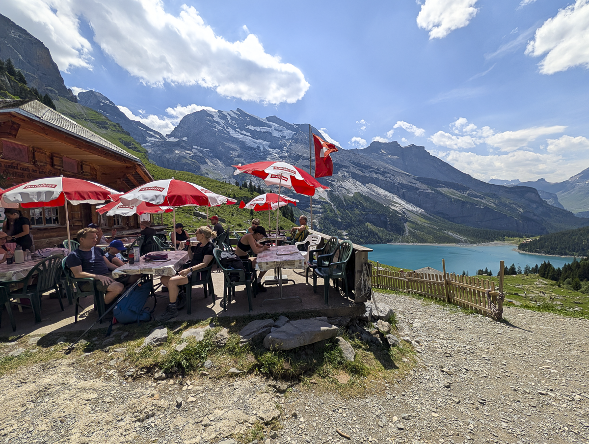 picnic tables with umbrellas next to a turquoise mountain lake